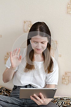 A young woman greets an online interlocutor. Woman communicates via tablet with her parents