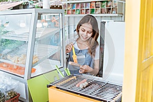 Young woman grilling a sausage and meetball