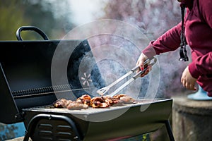 Young woman grills some kind of marinated meat and vegetable on gas grill during summer time, BBQ