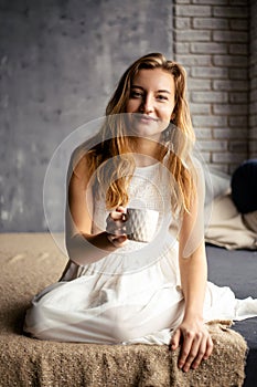 The young woman grins, cradling a coffee mug in her hands. The image captures the essence of the morning coffee ritual