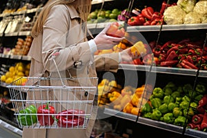 young woman with a grocery basket in a supermarket chooses fresh vegetables