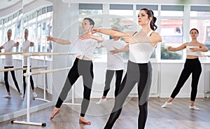 Young woman in group lesson with students rehearses, practices ballet dance, staging.