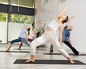 Young woman with group of sporty adult girls training stretching workout in yoga studio