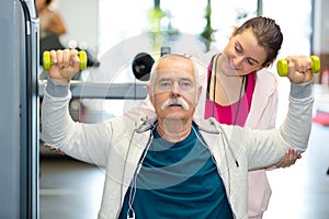 young woman guiding senior man to lift weights