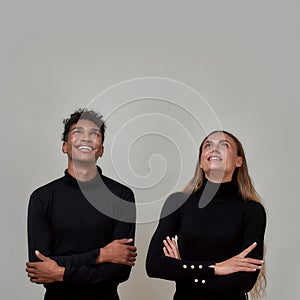 Young woman and guy dressed elegantly in black looking up excited, promoting something while standing together with arms