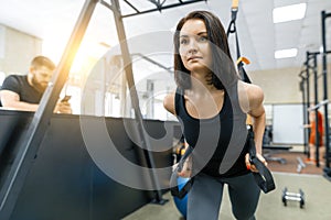 Young woman at the gym doing fitness exercises using sports straps system, holding hands by the loops. Fitness, sport, training,