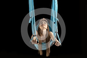 Young woman gymnast hovers in the air in sports hammock. Portrait of woman during yoga training on black background