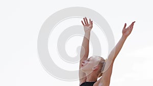 A young woman gymnast stands on the high bars on the beach on her training