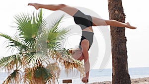 A young woman gymnast uses high bars on the beach for her training - doing a handstand