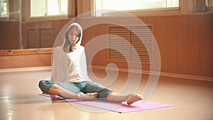 Young woman gymnast warming up sitting on the floor and doing leg exercises