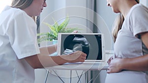 Young woman gynecologist doctor showing to pregnant woman ultrasound scan baby with digital tablet in medical consultatio