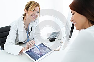 Young woman gynecologist doctor showing to pregnant woman ultrasound scan baby with digital tablet in medical consultation