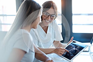 Young woman gynecologist doctor showing to pregnant woman ultrasound scan baby with digital tablet in medical consultation