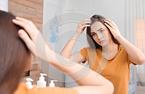 Young woman with hair loss problem looking in mirror