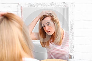 Young woman with hair loss problem near mirror