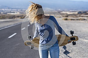 Young woman with hair moved from wind hidden face and long skate board walk free in outdoor leisure activity travel with long