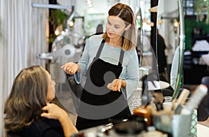 Young woman hair stylist talking to elderly female client in salon