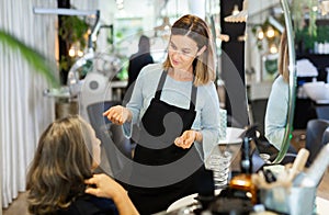 Young woman hairdresser discussing haircut with aged female client