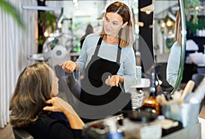 Young woman hairdresser discussing haircut with aged female client