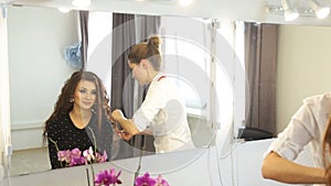 Young woman and hairdresser with hair iron making hairdo at hair salon