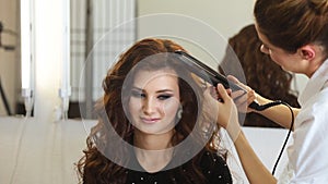 Young woman and hairdresser with hair iron making hairdo at hair salon