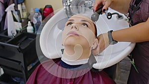 Young woman with hairdresser washing head at hair salon, after coloring the hair. Female hair stylist rinsing hair of