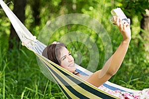 Young woman in a hammock in garden doing snapshot.