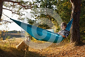 Young woman in hammok using laptop working outdoor facing lake on a sunset together with her home pet dog