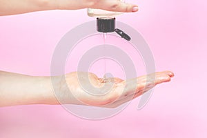 Young woman hand applying transparent alcohol gel to sanitize, clean and desinfect skin on pink background. Infection prevention photo