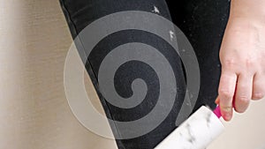 Young woman hand cleans stained black pants from white animal hair with lint removal roller