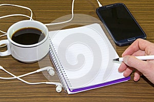 Young woman hand holding smartphone and pen writing on notebook paper at coffee shop.