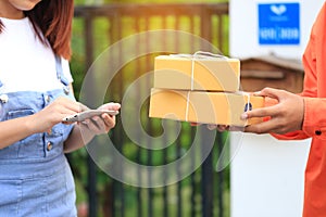 young woman hand holding smartphone and signing receipt of delivery package with delivery man bringing some package