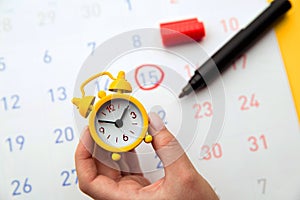 Young woman hand holding yellow clock. Calendar in background. Positive result. It is a time for baby.Gynecology concept