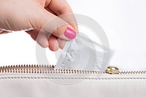 Young woman hand pulling a condom from a  leather bag, white background photo