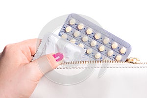 Young woman hand pulling a contraceptive pills blister and condom from a  leather bag, white background photo