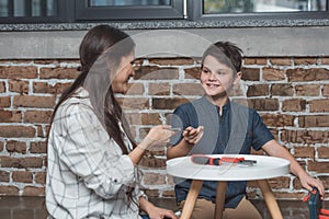 Young woman handing pliers to her little son while sitting on floor