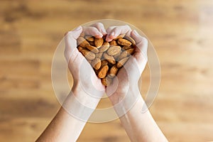 Young woman hands forming heart shape holding almonds nuts at home