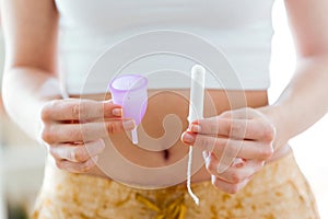 Young woman hands holding different types of feminine hygiene products - menstrual cup and tampons.