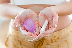 Young woman hands holding different types of feminine hygiene products - menstrual cup and tampons.