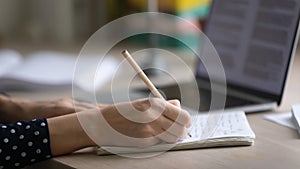 Young woman hands making notes in copybook by computer screen
