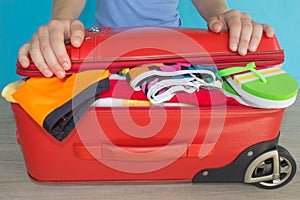 Young woman hands packing suitcase. Women& x27;s clothes and accessories in red suitcase things prepared for travel