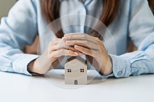 Young woman hands protecting miniature house, Home insurance concept