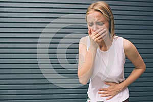 Young woman with hands on stomach having bad aches pain on gray background. Food poisoning, influenza, cramps