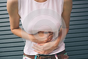 Young woman with hands on stomach having bad aches pain on gray background. Food poisoning, influenza, cramps