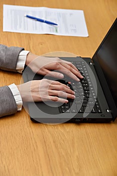 Young woman hands using laptop in a wood table, indoor. Women hands working with laptop, document on the background.
