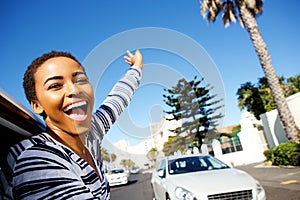 Young woman hanging outside car window with arms raised