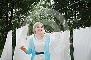 Young woman hangs white clean sheets in the garden. Domestic responsibilities. A woman smiles and catches soap bubbles.  Great