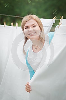 Young woman hangs white clean sheets in the garden. Domestic responsibilities of women