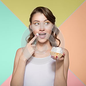 Young woman happily eating a sweet dessert. To bring a finger in a sweet cream to a mouth. Colorful bright background