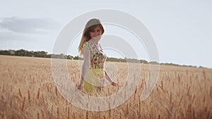 Young woman happily walks in the field, whirls and strokes the ears of the hand